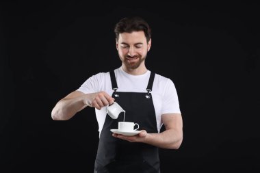 Gülümseyen barista siyah arka planda kahve yapıyor.