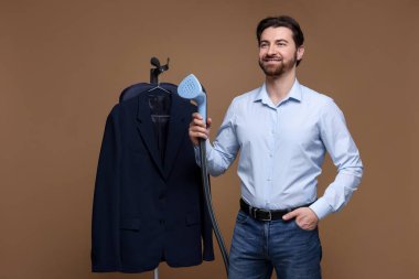 Kahverengi arka planda vapuru ve ceketi olan adam.