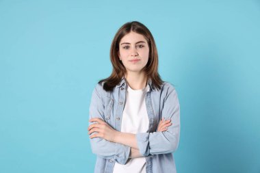 Açık mavi arka planda çapraz kollu güzel genç kız portresi