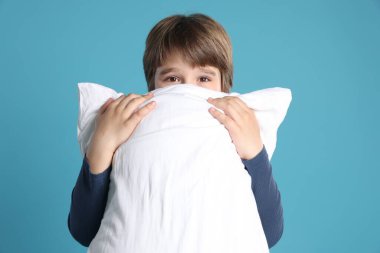 Açık mavi arka planda yastığı olan sevimli bir çocuk.