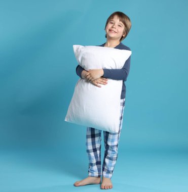 Açık mavi arka planda yastığı olan sevimli bir çocuk.