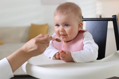 Anne, bebeğini sandalyeyle besliyor.