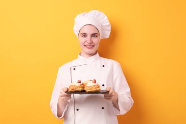 Üniformalı şekerci turuncu arka planda lezzetli profiteroller tutuyor.