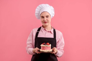 Şekerci pembe arka planda lezzetli bir pasta tutuyor.