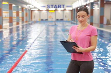 Yüzme koçu kapalı havuzda notlar alıyor. Metin için boşluk