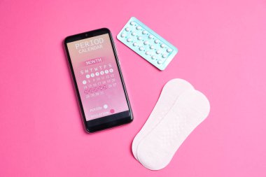Dönem takvimi uygulamalı akıllı telefon ve pembe arka planda adet ürünleri, düz yatış
