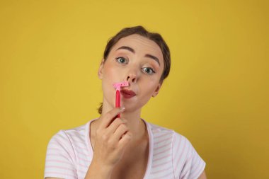 Güzel bir kadın, açık yeşil arka planda jiletle bıyığını tıraş ediyor.