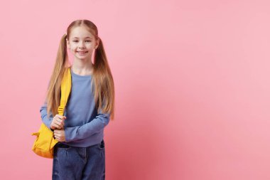 Pembe arka planda sırt çantası olan tatlı bir kız öğrenci. Metin için boşluk