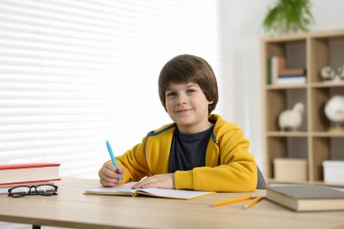 Evde, masada ödev yapan sevimli küçük çocuk.