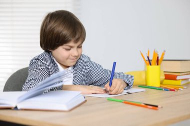 Evde, masada ödev yapan sevimli küçük çocuk.