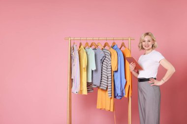 Gülümseyen moda stilisti, pembe arka planda tablet ve elbise askısı var. Metin için boşluk