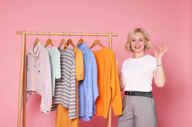 Gülümseyen moda tasarımcısı pembe arka planda güzel jest ve askılar gösteriyor.