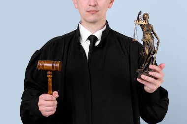 Gri arka planda Adalet Anıtı heykeli ve tokmakla yargıç, yakın plan.