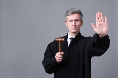 Elinde tokmak olan yargıç gri arkaplanda dur işareti yapıyor. Metin için boşluk