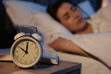 Evde uyuyan genç kadın, çalar saate ve kitaba odaklan.