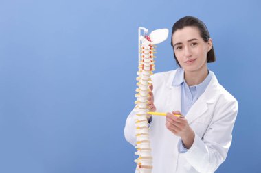 Doktor, mavi duvarın yakınındaki insan omurga modelini işaret ediyor. Metin için boşluk