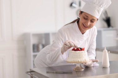 Pastacı mutfakta taze böğürtlenlerle pasta süslüyor.