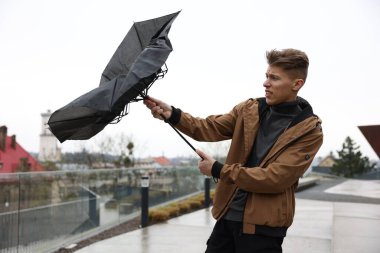 Kırık şemsiyeli bir adam açık havada yağmur altında rüzgarla savaşıyor.