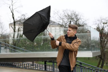 Kırık şemsiyeli bir adam açık havada yağmur altında rüzgarla savaşıyor.