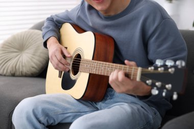 Genç adam kanepede gitar çalıyor, yakın plan.