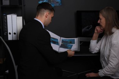 Adli tıp uzmanları ofiste olay yeri fotoğraflarıyla çalışıyorlar.