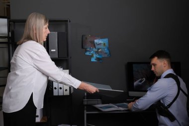 Adli tıp uzmanları ofiste olay yeri fotoğraflarıyla çalışıyorlar.