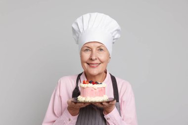 Açık gri arka planda pastası olan profesyonel bir pastacı.