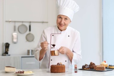 Gülümseyen pasta şefi mutfaktaki masada erimiş çikolatayla süsleme yapıyor.