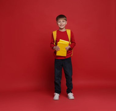 Sırt çantası ve kırmızı arka plan kitapları olan tatlı bir okul çocuğu.