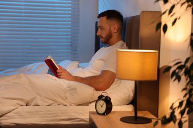 Genç adam evde yatakta kitap okumak