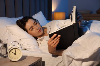 Evde yatakta kitap okuyan genç bir kadın.
