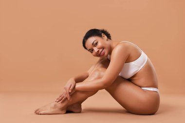 Beyaz iç çamaşırlı, pürüzsüz bir kadın. Bej arka planda epilasyon işleminden sonra.