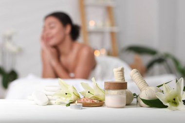 Güzel bir kadın masaj koltuğunda dinleniyor, farklı spa ürünlerine ve zambak çiçeklerine odaklanıyor.