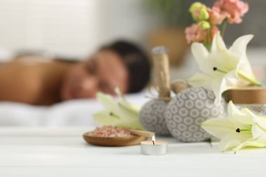 Güzel bir kadın masaj koltuğunda dinleniyor, farklı spa ürünlerine ve zambak çiçeklerine odaklanıyor.