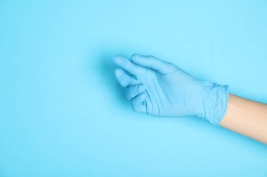 Açık mavi arka planda tıbbi eldiven giyen doktor, yakın plan. Metin için boşluk