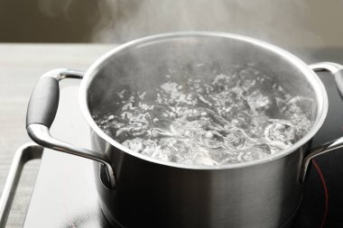 Kaynar suyla pişirme tenceresi ve soba gri arka planda, yakın plan