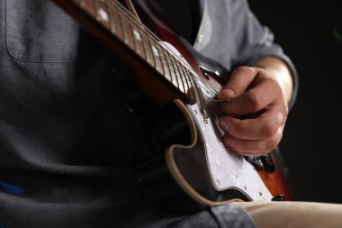 Siyah arkaplanda arabulucuyla gitar çalan adam, yakın plan