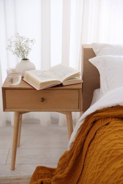 İçinde kitap olan komodin, vazoda çiçekler, yatağın yanında bir bardak su ve bardaklar.