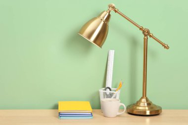 Lambalı, kırtasiyeli ve açık yeşil duvarın yanındaki ahşap masada kahveli şık bir iş yeri. Metin için boşluk