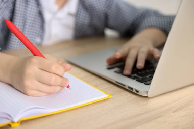 Küçük çocuk laptopuyla ev ödevi yapıyor, ahşap masada, yakın plan.