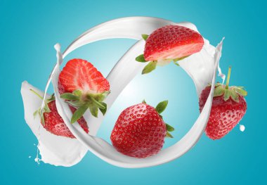 Süt sıçraması ve açık mavi arkaplanda taze çilekler.