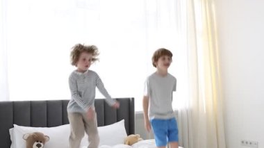 Küçük kardeşler evde yatakta birlikte zıplıyorlar.