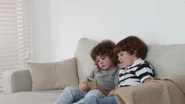 Evdeki kanepede akıllı telefonları olan şirin küçük kardeşler.