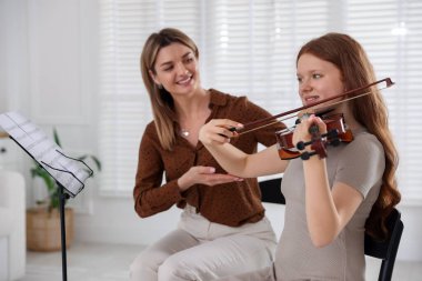 Genç bir kıza müzik dersinde keman çalmayı öğreten kadın.
