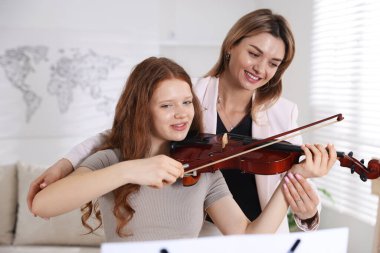 Genç bir kıza müzik dersinde keman çalmayı öğreten kadın.