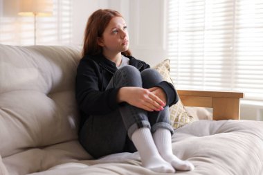 Evdeki kanepede oturan üzgün genç kız.