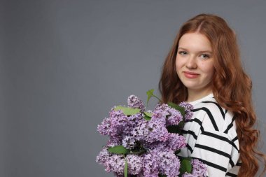 Gri arka planda bir demet leylak çiçeği olan güzel bir genç kız. Metin için boşluk