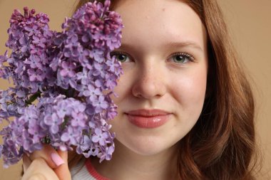 Bej arka planda leylak çiçekleri olan güzel genç kız, yakın plan.