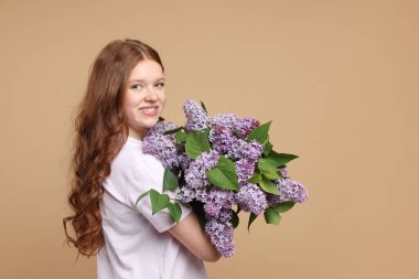 Bej arka planda bir demet leylak çiçeğiyle gülümseyen genç kız. Metin için boşluk
