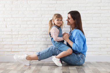 Güzel anne ve küçük kızı beyaz tuğla duvarın yanında. Metin için boşluk
